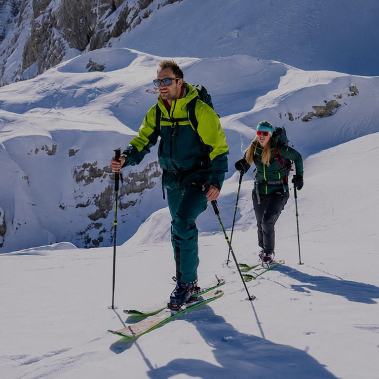 Two skiers trekking up a snowy mountain slope with professional winter gear