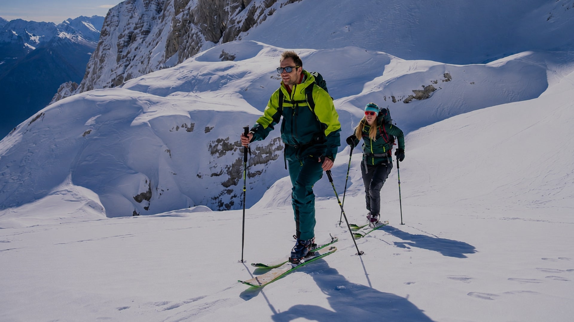 Two skiers trekking up a snowy mountain slope with professional winter gear