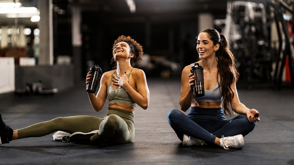 Woman sitting on gym floor drinking a healthy protein recovery shake