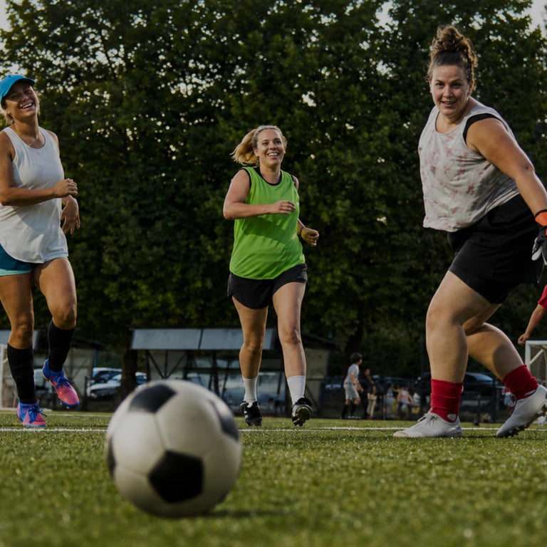 Group of women playing a competitive soccer game on green grass