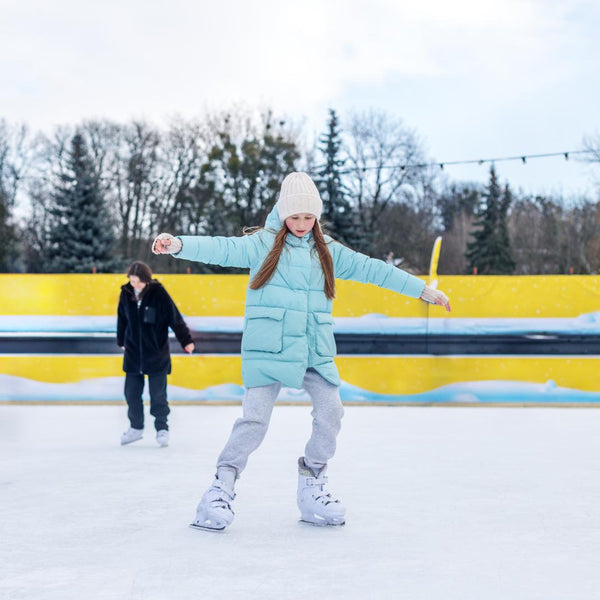 Young girl ice skating on an outdoor rink surrounded by winter trees